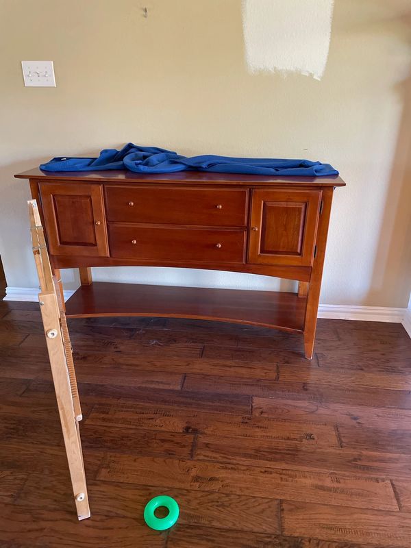 Wooden sideboard with a blue cloth on top and a green ring on the floor.