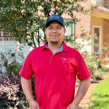 Man in a red polo shirt and black cap standing outdoors, smiling.