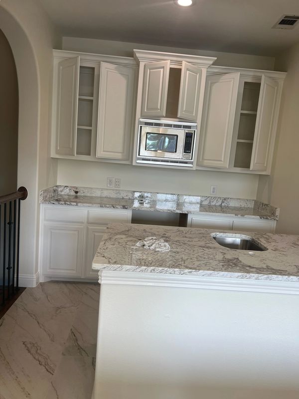Modern kitchen with white cabinets and marble countertops, featuring a built-in microwave.