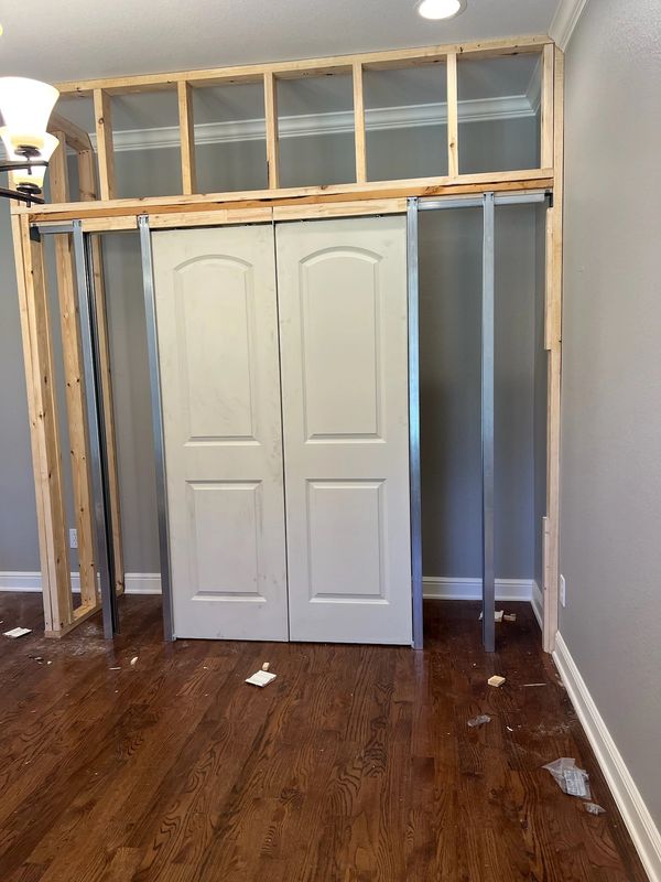 Partially constructed wall with sliding cabinet doors and wooden framing.