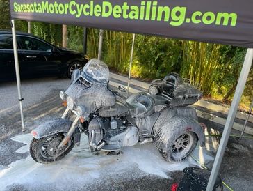 A motorcycle trike covered in soap under a Sarasota MotorCycle Detailing tent.