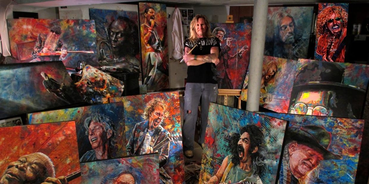 Artist stands among colorful paintings of famous musicians in a studio.