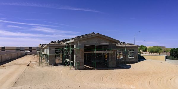House under construction with scaffolding and materials on the roof in a sandy area.