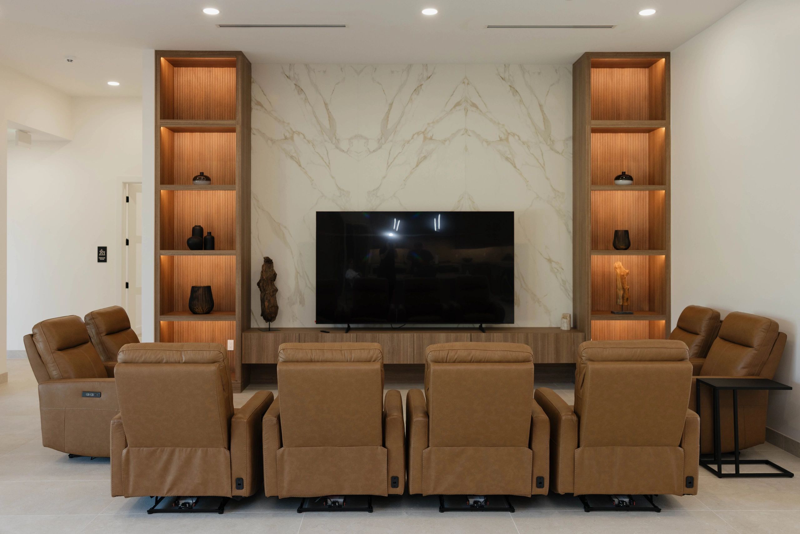 Modern living room with leather recliners and a large TV on a marble wall.