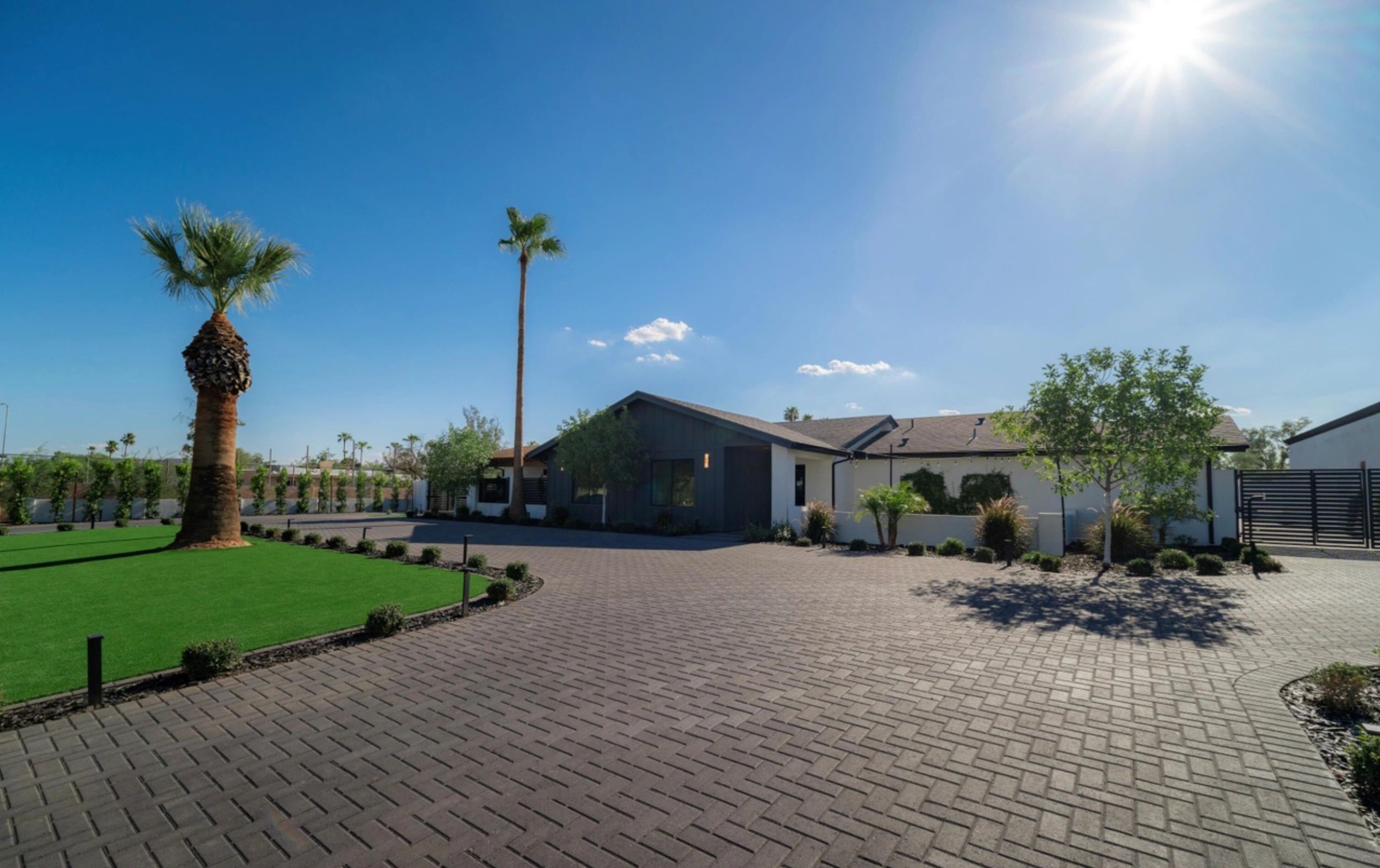 Modern house under bright sun with palm trees and a paved driveway.
