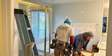 Two workers renovating a bathroom with tools and a ladder.