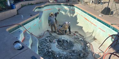 Workers breaking concrete inside an empty swimming pool under renovation.