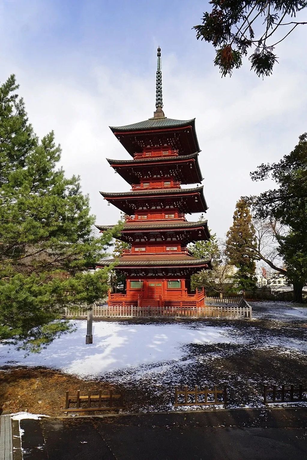 A traditional red pagoda in a snowy garden surrounded by trees.