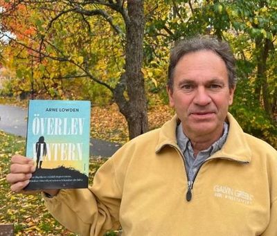 Man in yellow jacket holding a book titled 'Överlev Vinter'.