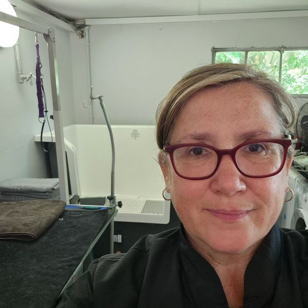 Woman with glasses smiling indoors near a window and some equipment.