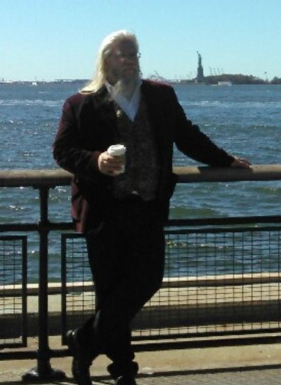 Man in a suit holding a paper cup leaning on railing near water Statue of Liberty in the background