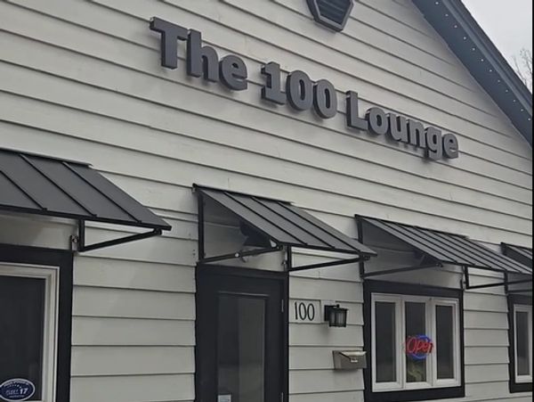 Exterior of The 100 Lounge with black awnings and an open sign.