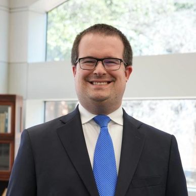 Smiling man in glasses and a blue tie in an office setting.
