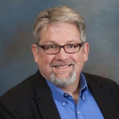 Smiling middle-aged man with glasses and a beard in a black jacket.