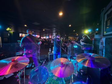 Band performs live on stage viewed from behind the drums.