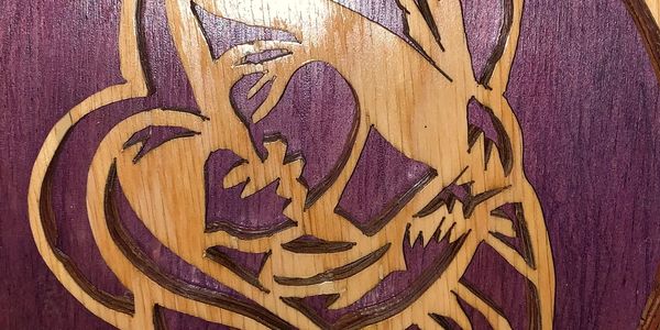 Wooden carving of a smiling cartoon mouse on a purple background.