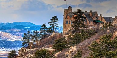 Cherokee Ranch castle on hillside, Colorado mountain in background, pine trees in foreground ranch.