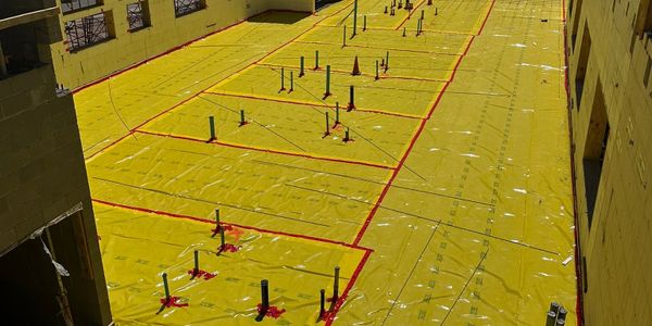 Construction site with yellow waterproofing membrane and marked areas.