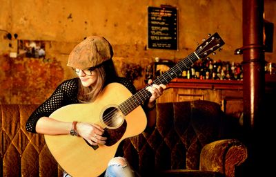 Woman playing guitar indoors with a smile.