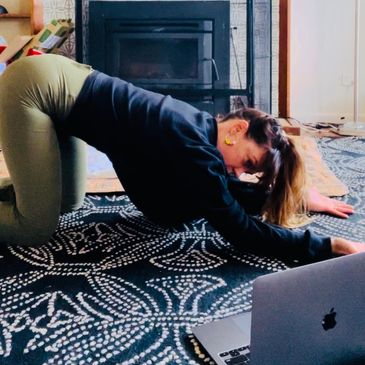 Woman stretching on floor while watching online movement class - pre-natal and post-natal movement