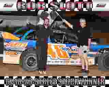 Two people with a race car at night posing with a trophy.