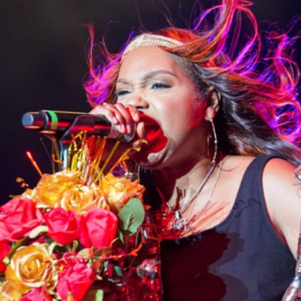 Woman passionately singing on stage with bouquet and vibrant lighting.