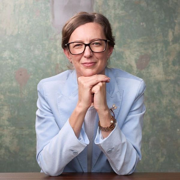 Confident woman in glasses and light blue blazer, smiling gently.