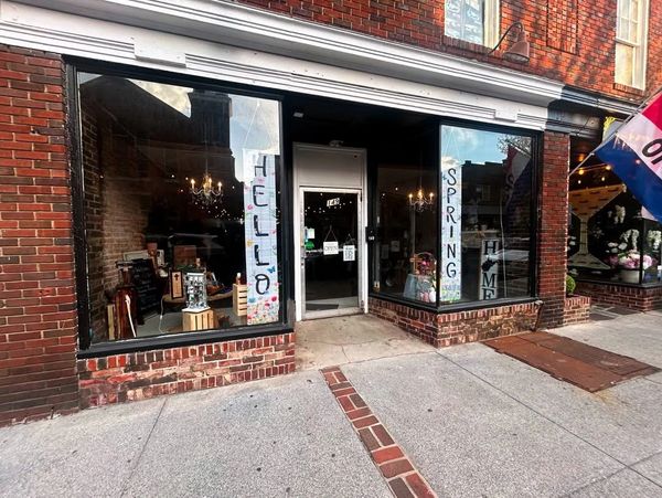 Charming brick storefront with large windows displaying home decor and seasonal spring signs.