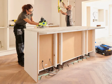 Two people installing kitchen cabinets and countertops in a bright home.
