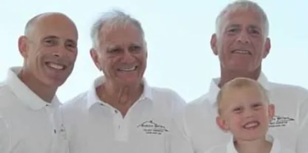 Four males of different generations smiling together in white shirts.