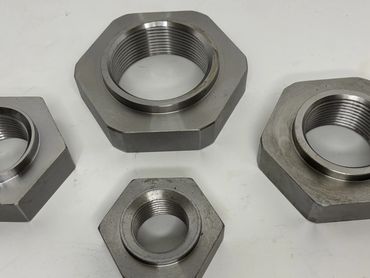 Four large hexagonal metal nuts with internal threading on a white surface.