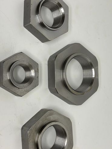 Four metallic hexagonal nuts with internal threading on a white surface.