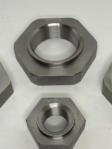 Two large hexagonal metal nuts with internal threading on a white surface.