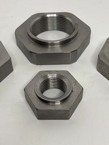 Two hexagonal metal nuts with internal threading placed on a white surface.