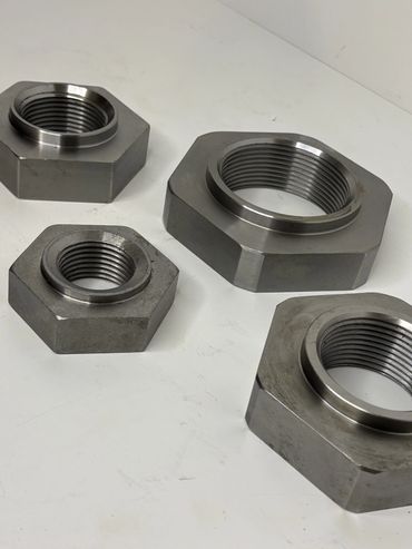 Four large hexagonal metal nuts with internal threading on a white surface.