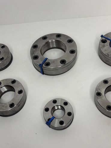Metal industrial flange fittings with bolts arranged on a white surface.