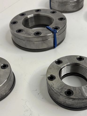 Metal threaded rings with bolt holes arranged on a white surface.