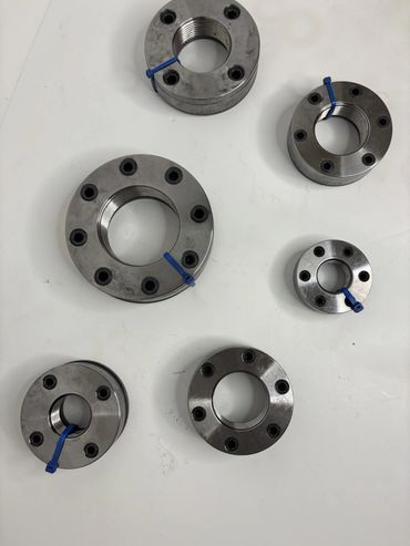 Six metallic industrial components with threaded centers and blue markers on a white surface.