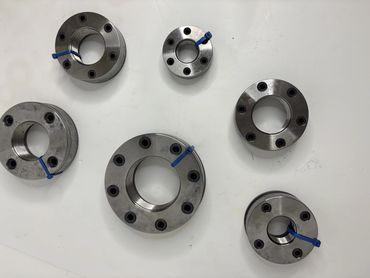 Six metallic industrial components with threaded centers and blue markers on a white surface.