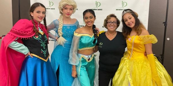 Five people posing, three dressed as Disney princesses, one in black.