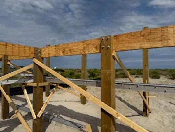 Wooden structure under construction on a sandy beach with ocean in the background.
