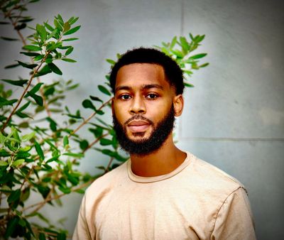 Portrait of a man with a beard against a plant and wall.