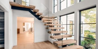 Modern floating wooden staircase with glass railing in a bright living space.