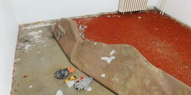 Room mid-renovation with old carpet partially removed and tools laid out.