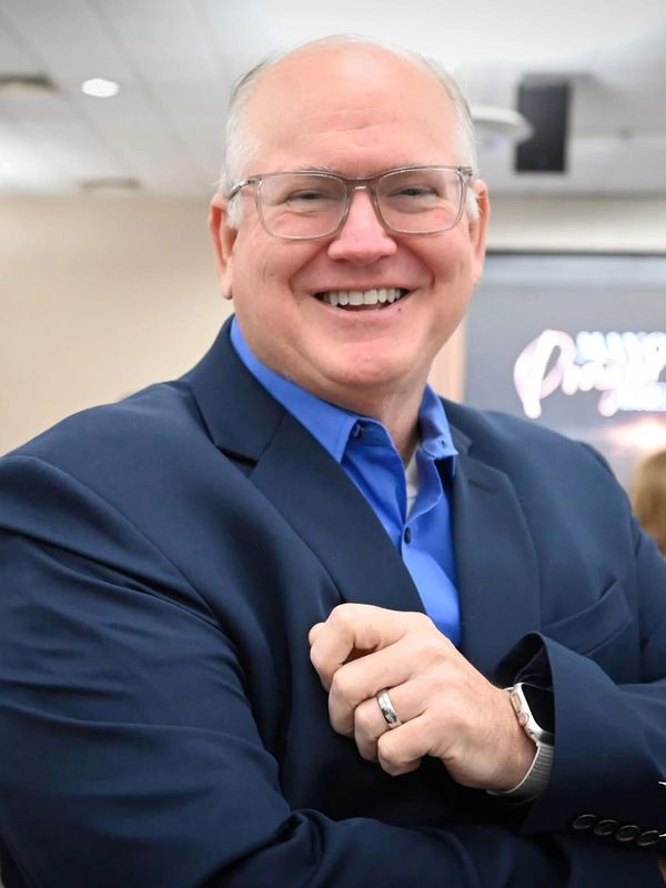 Smiling man in glasses and blue suit with crossed arms.