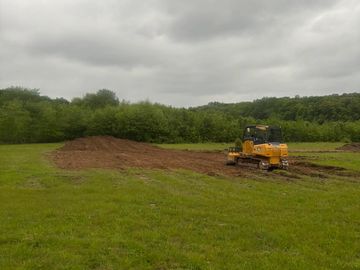 A yellow bulldozer leveling dirt in a grassy field under a cloudy sky.