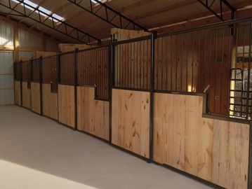 Row of wooden horse stalls with metal bars in a barn.