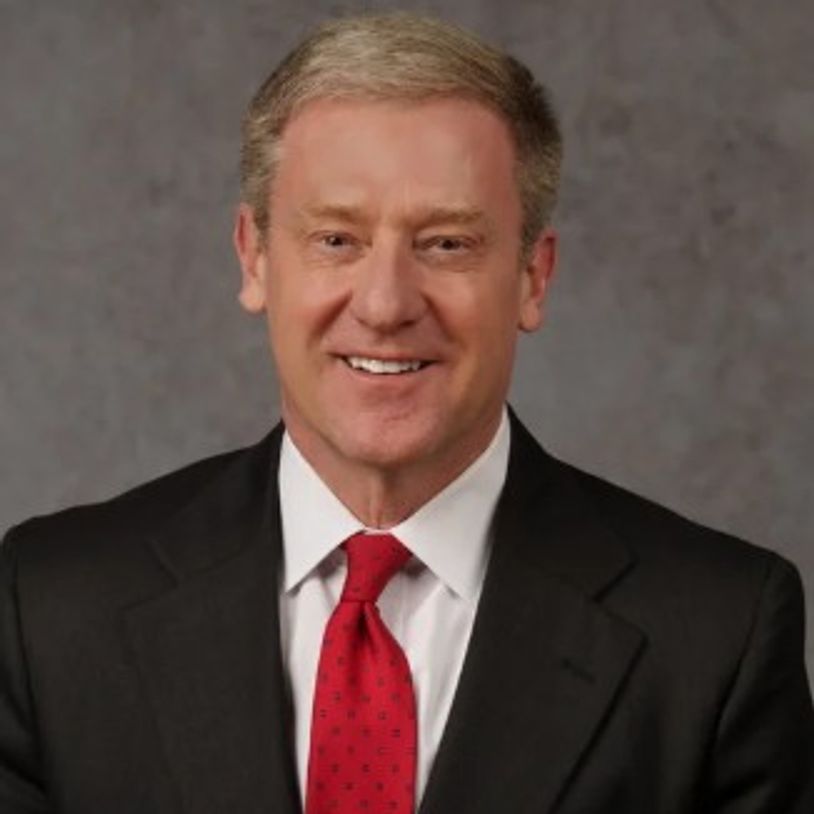 Smiling man in suit and red tie against gray background.