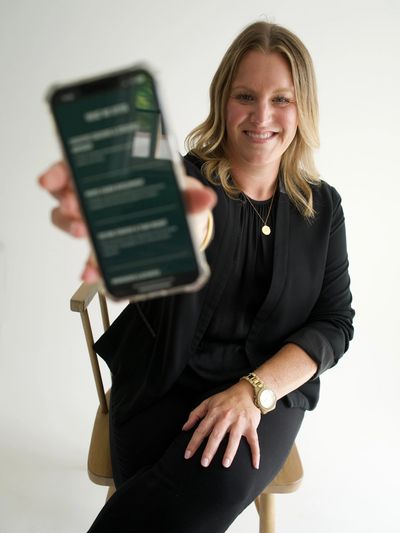 Katie Spidle sitting in chair holding cell phone with Elevate People Partner website loaded