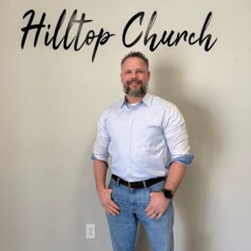 Man standing in front of a Wall with Hilltop Church sign.